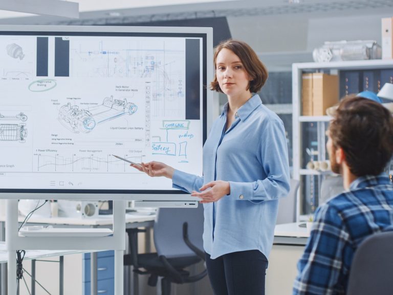 woman standing by a large screen showing automotive parts leading a meeting